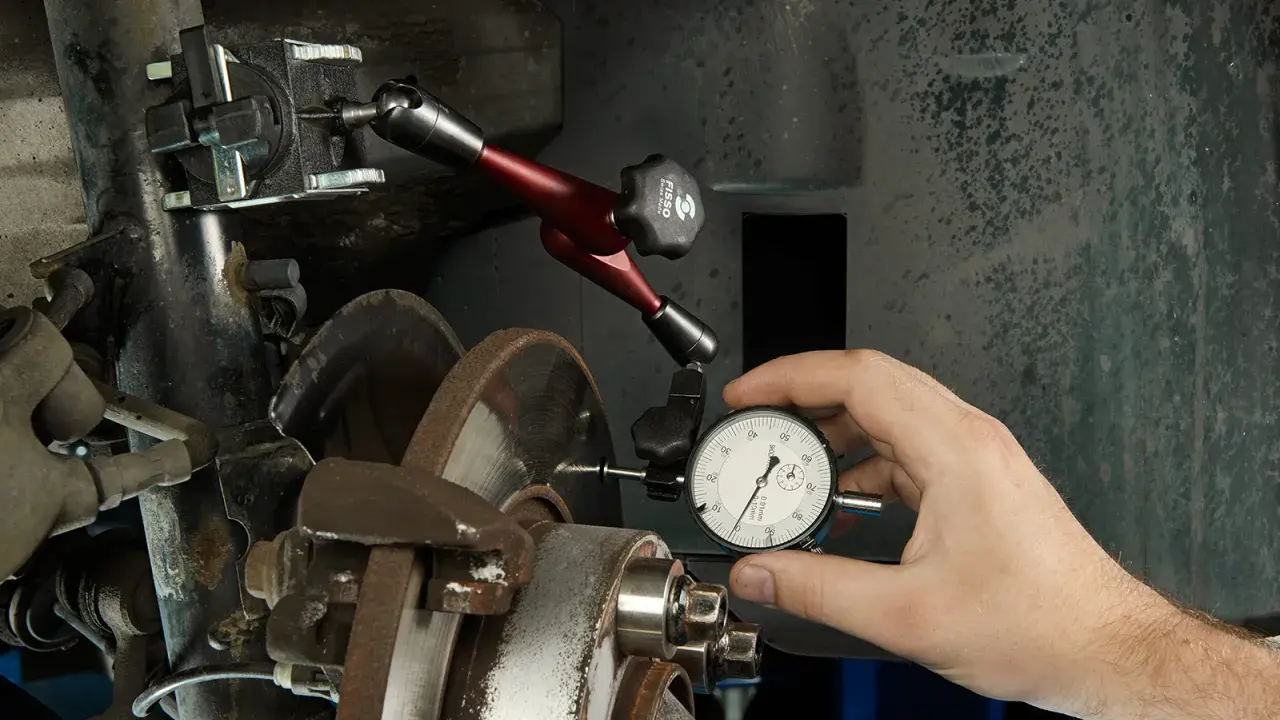 Mechanik mierzy bicie tarczy hamulcowej, by zdiagnozować drgania kierownicy przy hamowaniu.