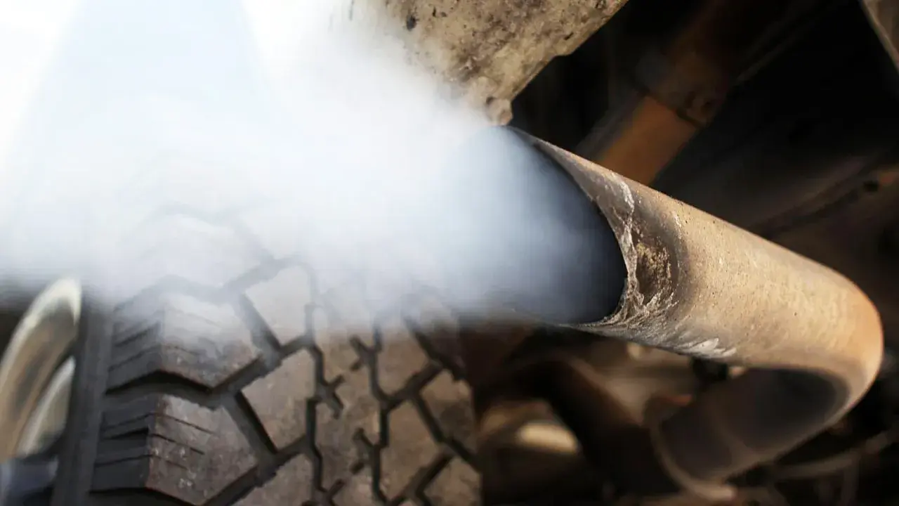 Biały dym z wydechu diesel wydobywa się z rury, zasłaniając fragment opony.