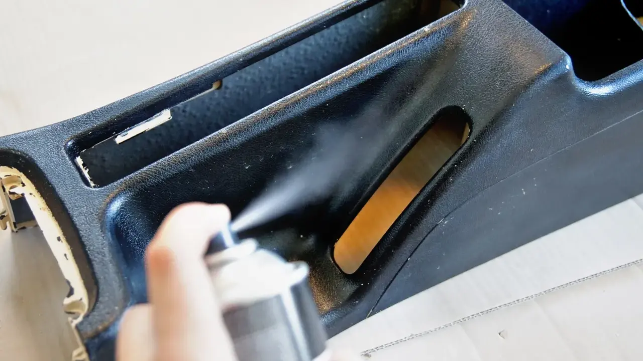 Ręka trzyma puszkę z farbą w sprayu, malowanie elementu konsoli środkowej samochodu.
