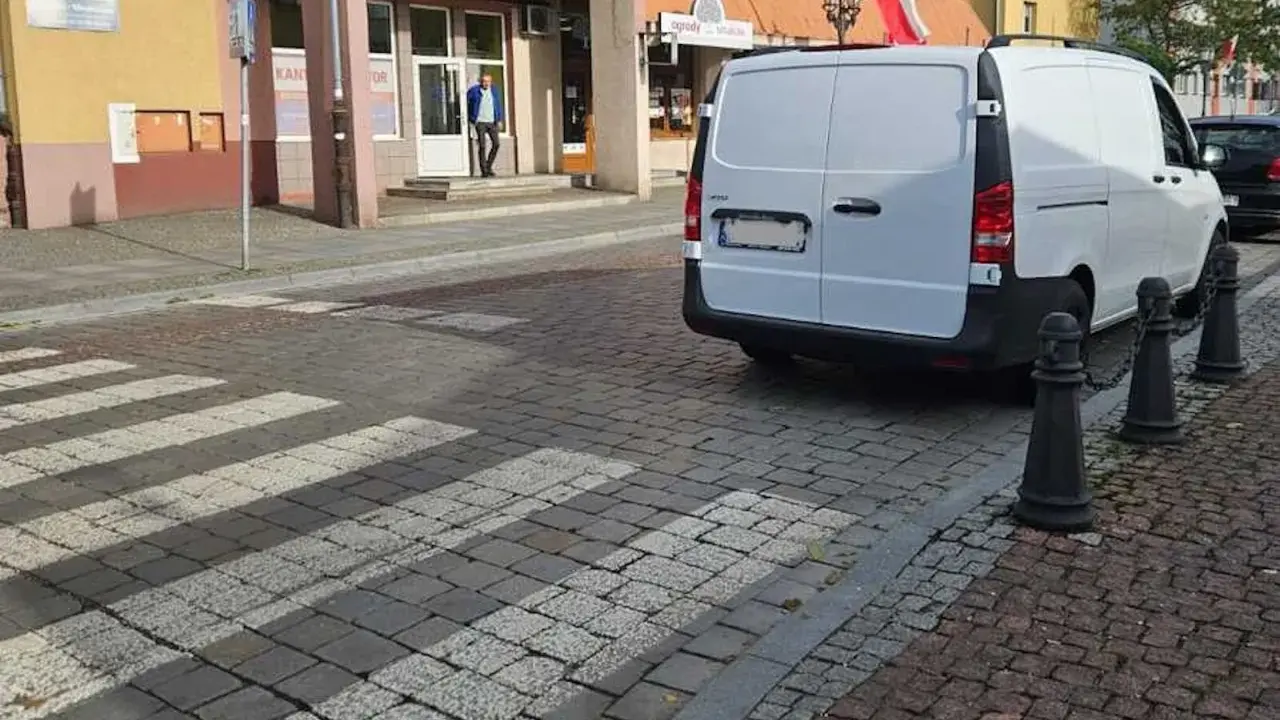 Biały van blokuje przejście dla pieszych na brukowanej ulicy.