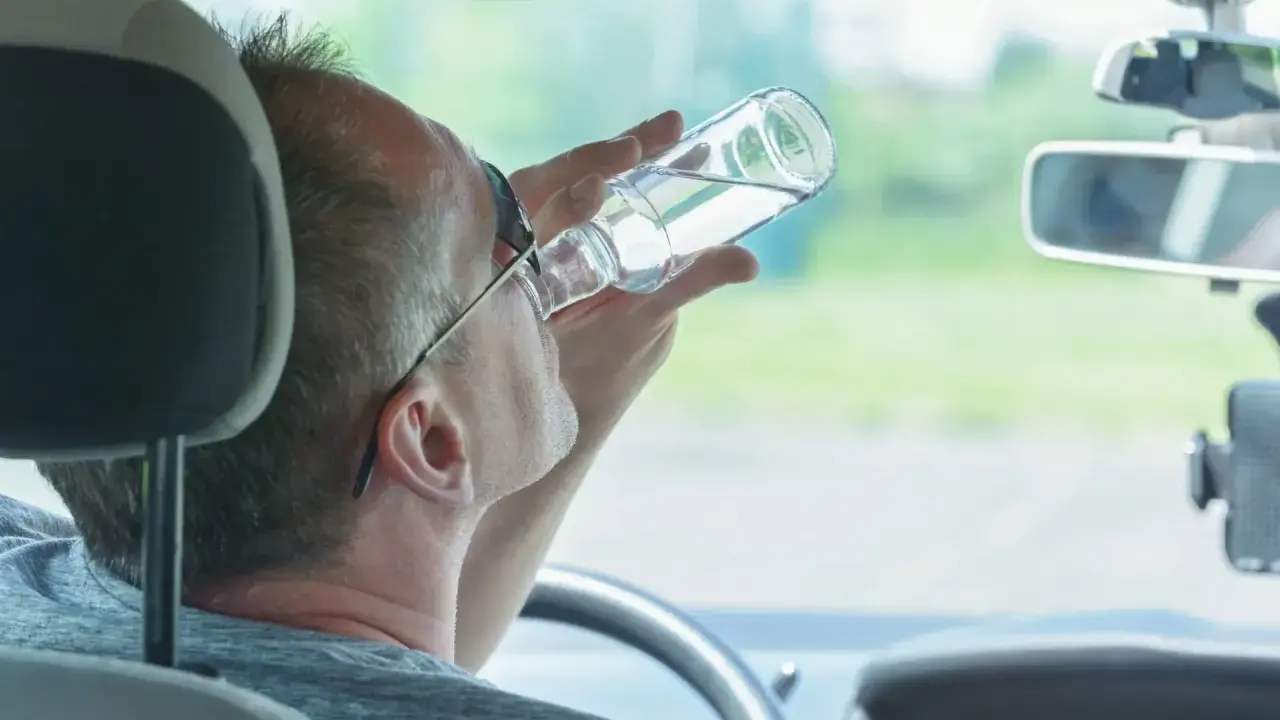 Mężczyzna pije alkohol za kierownicą. Pamiętaj, jaka kara za jazdę pod wpływem alkoholu jest surowa.