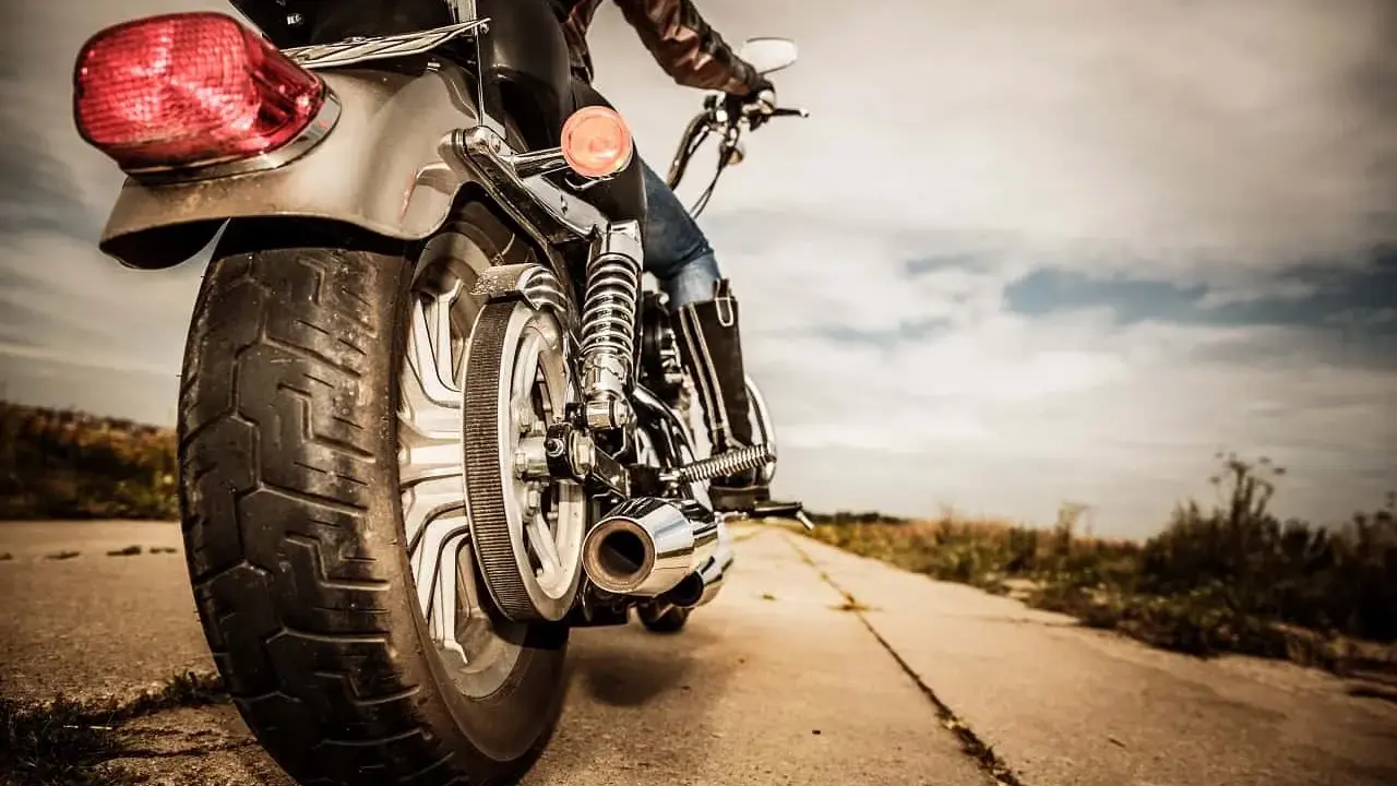 Osoba na motocyklu, widok z tyłu. Błyszczące chromy, skórzana kurtka i dżinsy. Droga prowadzi w dal, pod chmurami.