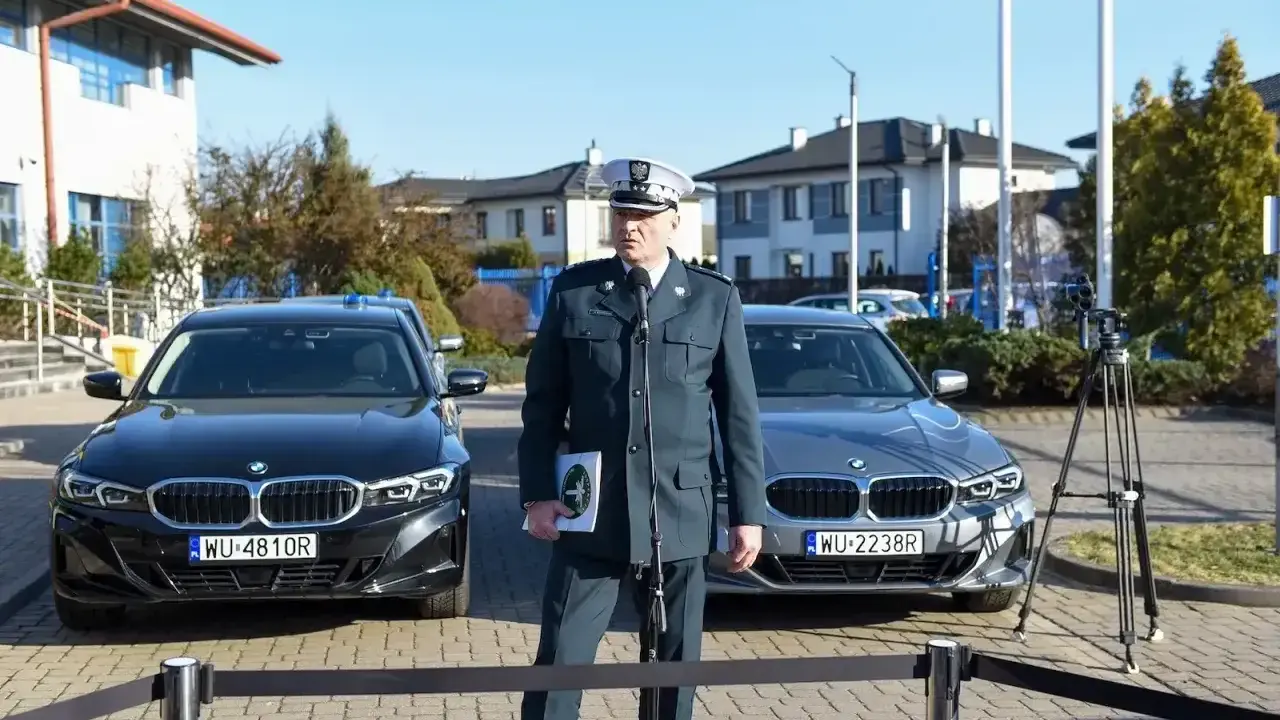 Funkcjonariusz w mundurze stoi między dwoma nieoznakowanymi radiowozami BMW.