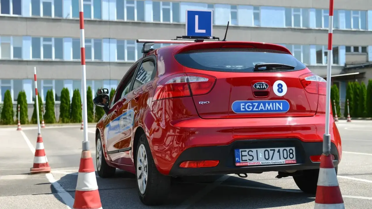 Czerwony samochód z literą "L" na dachu i napisem "EGZAMIN" na klapie. Na placu manewrowym, gdzie można sprawdzić, ile błędów można zrobić na egzaminie teoretycznym na prawo jazdy.