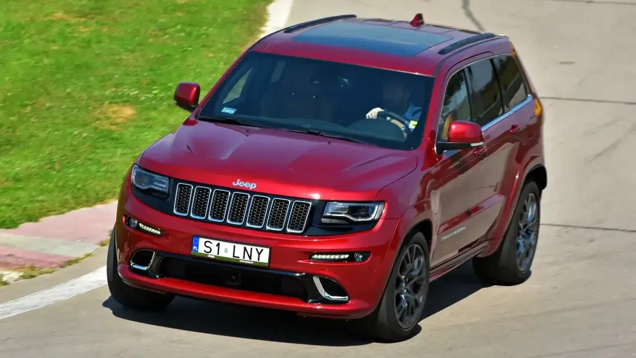 Czerwony Jeep Grand Cherokee z indywidualną tablicą rejestracyjną "S1 LNY" na torze wyścigowym.