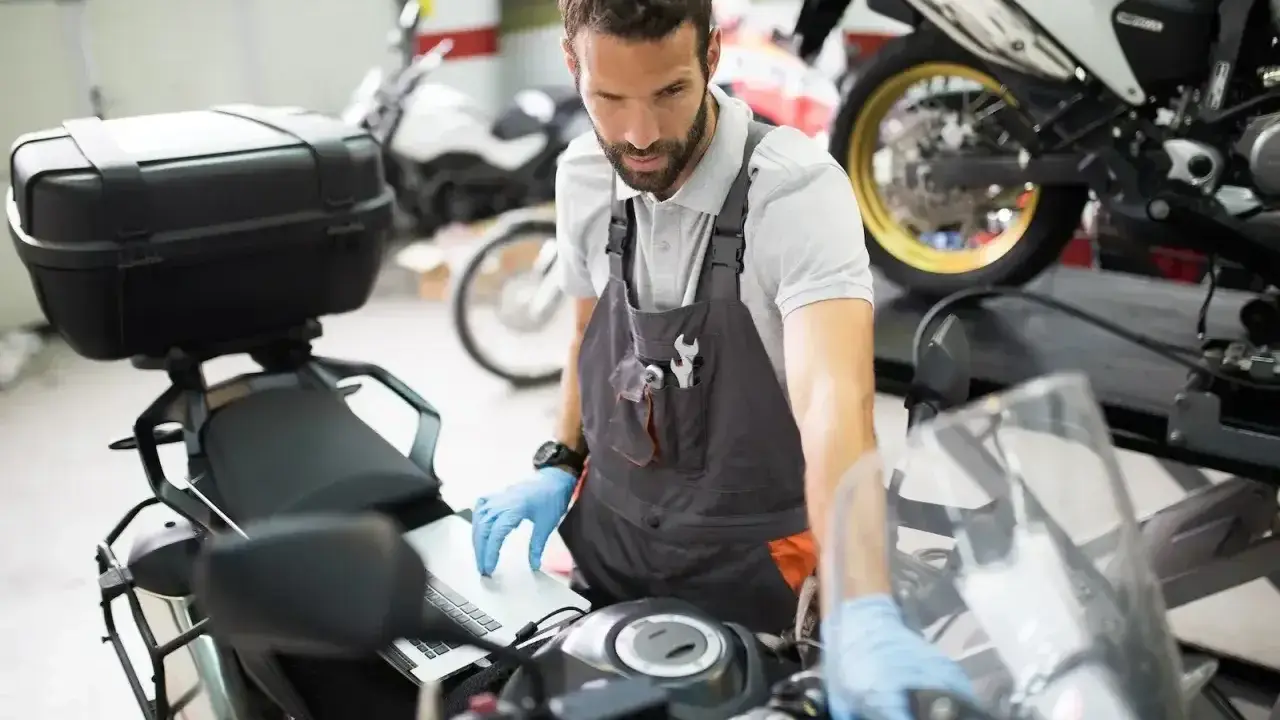 Mechanik w warsztacie sprawdza przegląd motocykla po terminie, używając laptopa do diagnostyki.