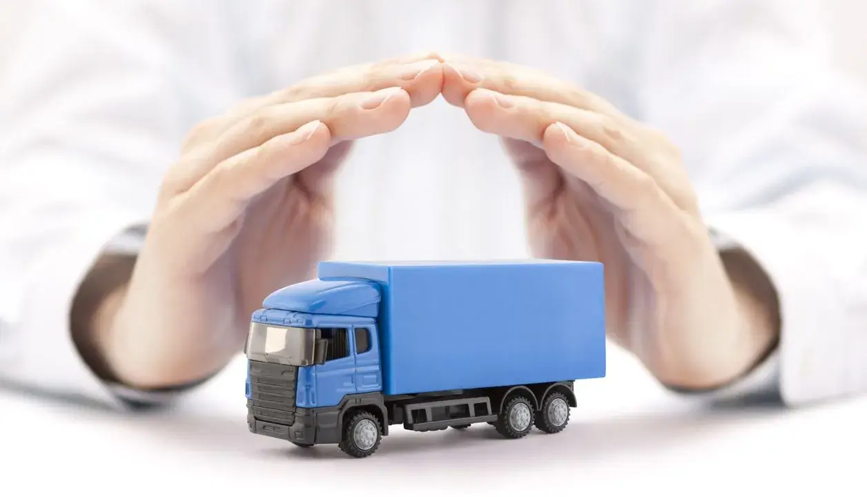 Ręce chronią niebieską ciężarówkę, symbolizując ubezpieczenie AC w kosztach transportu.