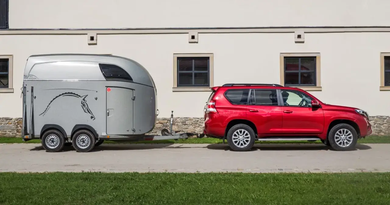 Czerwony SUV holuje przyczepę kempingową z wizerunkiem konia. Jaka kategoria na auto? To idealny zestaw do transportu zwierząt.