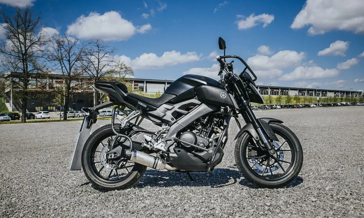 Czarny motocykl Yamaha, idealny na pierwsze prawo jazdy a1, stoi na żwirowym placu przed budynkiem.