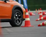 Pomarańczowy samochód na placu manewrowym, otoczony pachołkami. Może to być przygotowanie do obowiązkowej wymiany prawa jazdy.