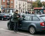 Mężczyzna przy samochodzie sprawdza telefon. UFG identyfikacja OC jest ważna dla każdego kierowcy.