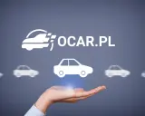 Dłoń trzyma symbol samochodu, nad którym widnieje logo OCAR.PL. To miejsce, gdzie znajdziesz ogólne warunki ubezpieczenia.
