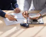 Dwóch mężczyzn analizuje dokumenty, kluczyki do auta i kalkulator. Rozważają podwójne ubezpieczenie OC.