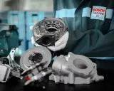 Mechanik w rękawiczkach prezentuje części do regeneracji turbo. W tle logo Bosch Service.