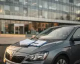 Szara Skoda na tle nowoczesnego biurowca. Na masce leżą dokumenty i długopis, gotowe do podpisania umowy OC na 30 dni.