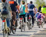 Grupa rowerzystów jedzie w kolumnie, przestrzegając przepisów. Widać plecaki i kamizelki odblaskowe.