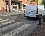 Biały van blokuje przejście dla pieszych na brukowanej ulicy.