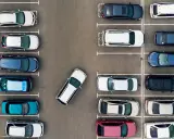 Widok z góry na parking z wieloma samochodami. Jeden biały samochód jest zaparkowany tyłem, pokazując, jak parkować tyłem.
