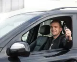 Szczęśliwy młody mężczyzna w czarnej skórzanej kurtce trzyma kluczyki do nowego auta, świeżo po rejestracji pojazdu z Niemiec.