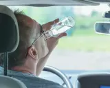 Mężczyzna pije alkohol za kierownicą. Pamiętaj, jaka kara za jazdę pod wpływem alkoholu jest surowa.