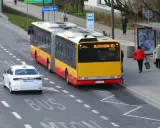 Autobus linii 182 zbliża się do przystanku, a biała taksówka czeka, by ustąpić mu pierwszeństwa.