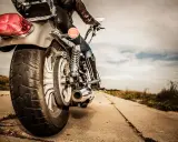 Osoba na motocyklu, widok z tyłu. Błyszczące chromy, skórzana kurtka i dżinsy. Droga prowadzi w dal, pod chmurami.