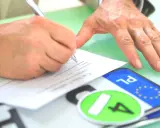 Podpisanie umowy kupna-sprzedaży pojazdu, co jest kluczowe dla uzyskania homologacji. Obok dokumentów leżą tablice rejestracyjne.