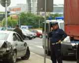 Policjant rozmawia przez radio przy miejscu wypadku. Uszkodzone auto i ciężarówka sugerują, że mogło dojść do zdarzenia związanego z pzu klauzula alkoholowa.
