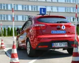 Czerwony samochód z literą "L" na dachu i napisem "EGZAMIN" na klapie. Na placu manewrowym, gdzie można sprawdzić, ile błędów można zrobić na egzaminie teoretycznym na prawo jazdy.
