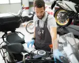 Mechanik w warsztacie sprawdza przegląd motocykla po terminie, używając laptopa do diagnostyki.
