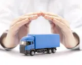 Ręce chronią niebieską ciężarówkę, symbolizując ubezpieczenie AC w kosztach transportu.