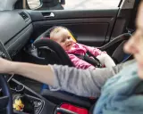 Uśmiechnięte dziecko w foteliku z przodu. Od kiedy dziecko może jeździć z przodu, zależy od jego wieku i wagi.
