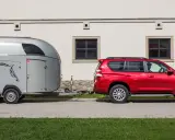 Czerwony SUV holuje przyczepę kempingową z wizerunkiem konia. Jaka kategoria na auto? To idealny zestaw do transportu zwierząt.