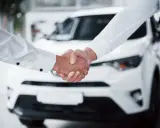 Uścisk dłoni na tle białego samochodu. Klient cieszy się z zakupu, mimo że brak karty pojazdu przy zakupie.