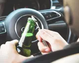 Ręce otwierające butelkę piwa za kierownicą. Pamiętaj, że od 0,2 promila zabierają auto.