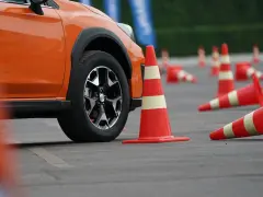 Pomarańczowy samochód na placu manewrowym, otoczony pachołkami. Może to być przygotowanie do obowiązkowej wymiany prawa jazdy.