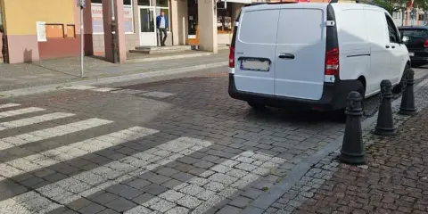 Biały van blokuje przejście dla pieszych na brukowanej ulicy.