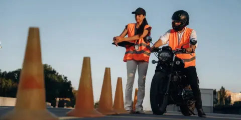 Instruktorka motocyklowa obserwuje kursanta podczas ćwiczeń na placu. Zastanawiasz się, ile godzin jazdy na kat. A potrzeba, by zdać egzamin?