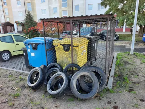 Kilka zużytych opon leży przed śmietnikami.