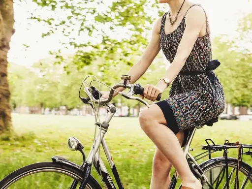 Kobieta w letniej sukience cieszy się przejażdżką rowerową po parku.
