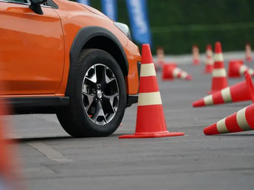 Pomarańczowy samochód na placu manewrowym, otoczony pachołkami. Może to być przygotowanie do obowiązkowej wymiany prawa jazdy.