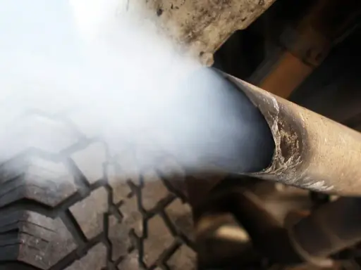 Biały dym z wydechu diesel wydobywa się z rury, zasłaniając fragment opony.