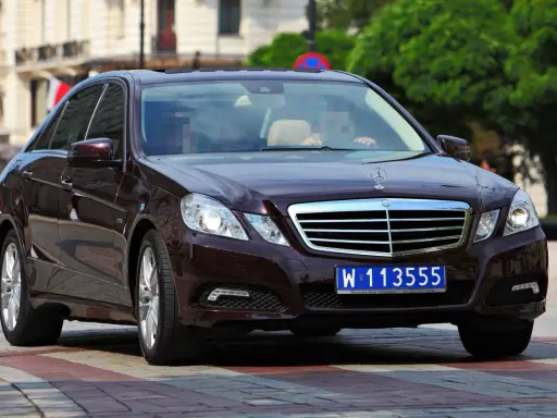 Ciemnobrązowy Mercedes z tablicami dyplomatycznymi W 113555, jadący po ulicy.