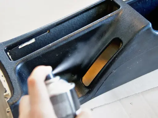 Ręka trzyma puszkę z farbą w sprayu, malowanie elementu konsoli środkowej samochodu.