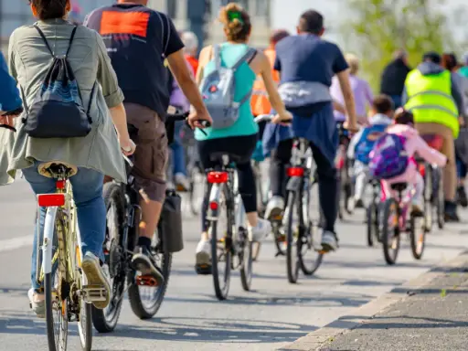 Grupa rowerzystów jedzie w kolumnie, przestrzegając przepisów. Widać plecaki i kamizelki odblaskowe.