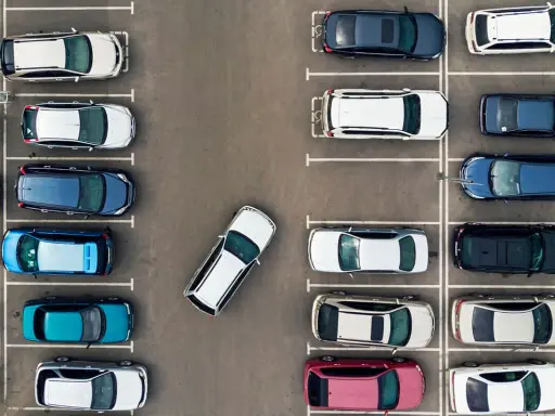 Widok z góry na parking z wieloma samochodami. Jeden biały samochód jest zaparkowany tyłem, pokazując, jak parkować tyłem.