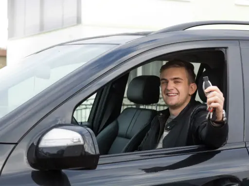 Szczęśliwy młody mężczyzna w czarnej skórzanej kurtce trzyma kluczyki do nowego auta, świeżo po rejestracji pojazdu z Niemiec.