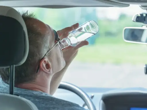 Mężczyzna pije alkohol za kierownicą. Pamiętaj, jaka kara za jazdę pod wpływem alkoholu jest surowa.