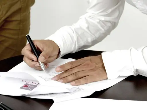 Mężczyzna podpisuje dokumenty, stając się ubezpieczającym dla ubezpieczonego. Na papierze widoczne logo firmy.