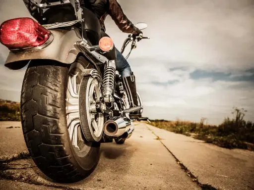 Osoba na motocyklu, widok z tyłu. Błyszczące chromy, skórzana kurtka i dżinsy. Droga prowadzi w dal, pod chmurami.